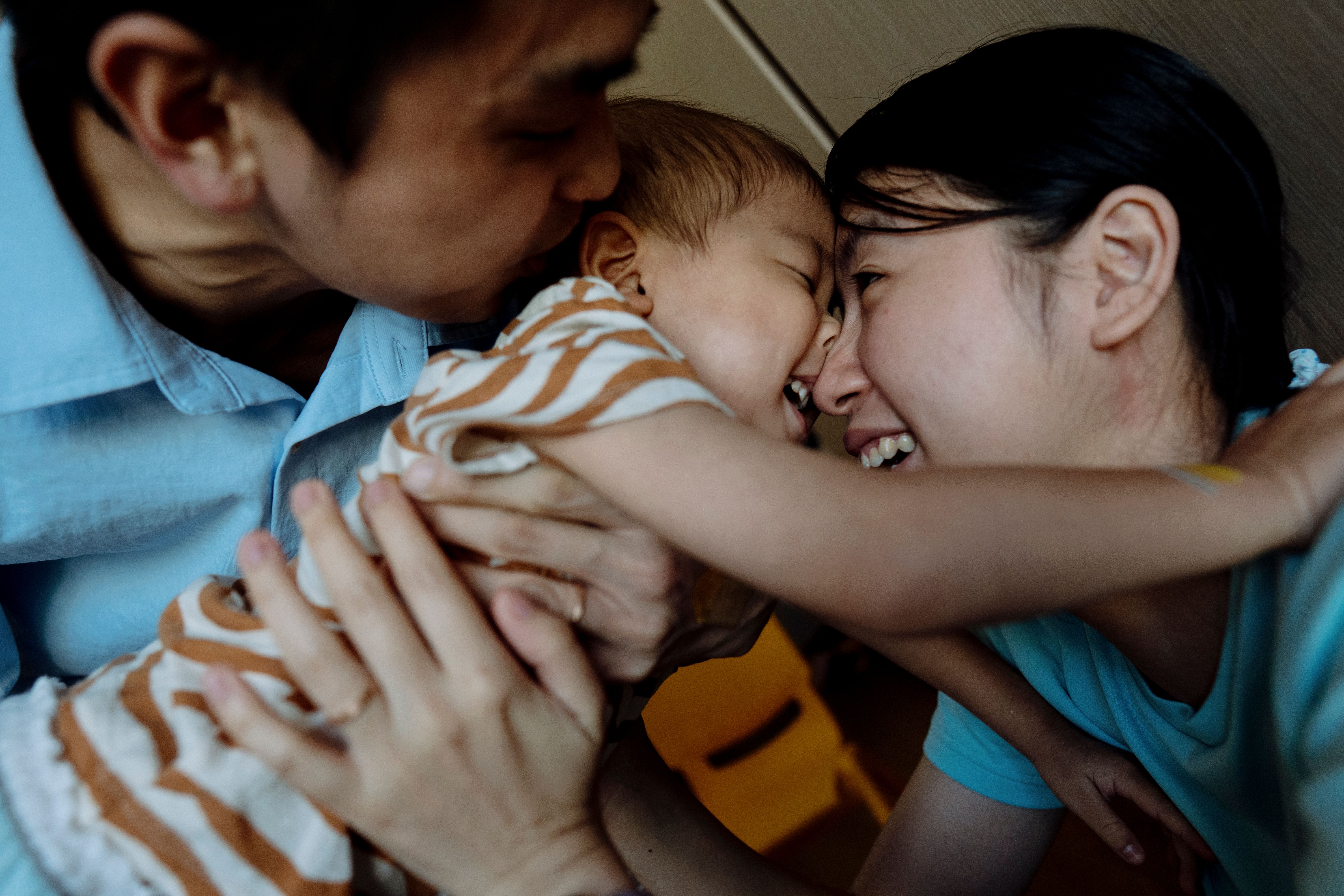 Parents cradling and nuzzling their laughing baby.
